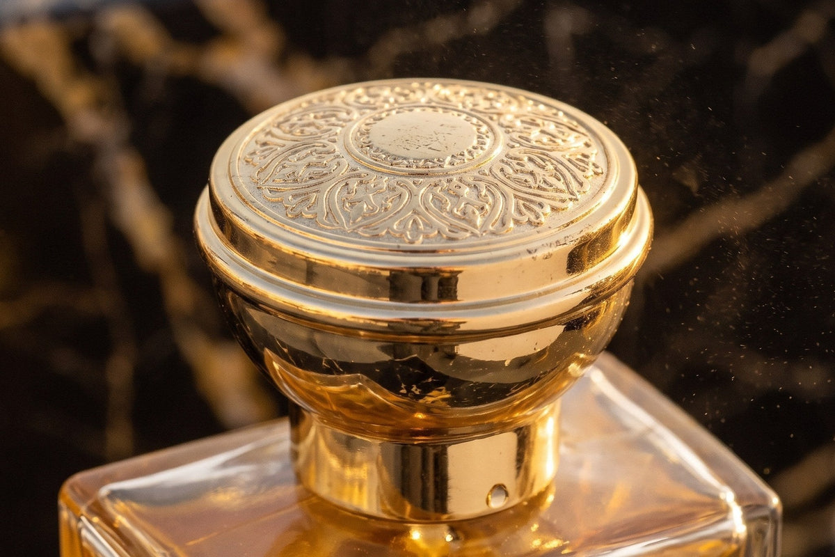 Capacul auriu, gravat, al parfumului Oud Al Amir Elixir, de aproape, pe marmură neagră