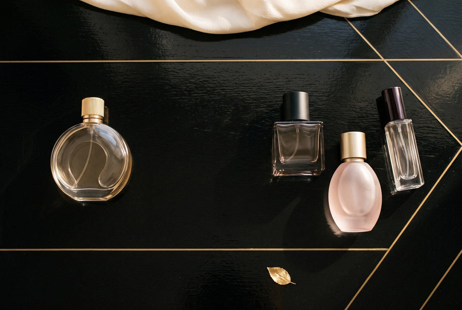 Un parfum individual și un grup de trei parfumuri, așezate separat pe o masă neagră cu detalii aurii.
